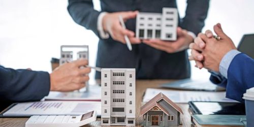 A professional businessman in a suit conducts a meeting at a desk while showcasing a model of a condominium or apartment building, discussing real estate development plans..shutterstock
